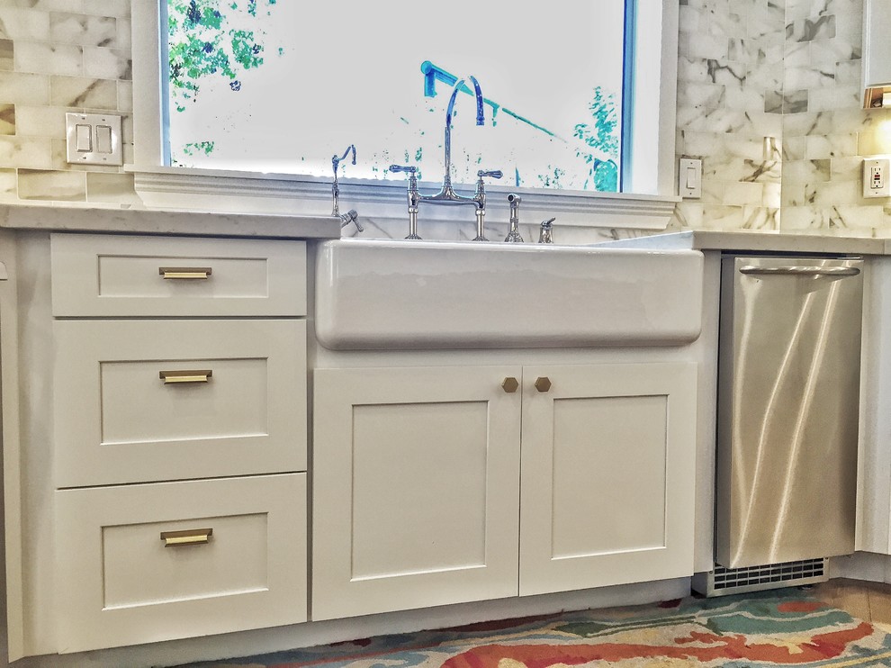 Klassisk inredning av ett stort vit vitt kök, med en rustik diskho, skåp i shakerstil, vita skåp, bänkskiva i kvarts, vitt stänkskydd, stänkskydd i marmor, rostfria vitvaror, laminatgolv, en köksö och beiget golv