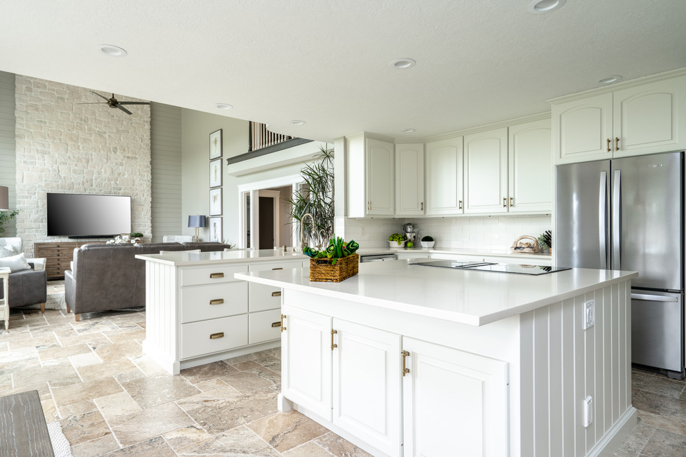 Design ideas for a traditional u-shaped open plan kitchen in Seattle with a submerged sink, raised-panel cabinets, white cabinets, engineered stone countertops, white splashback, porcelain splashback, stainless steel appliances, travertine flooring, an island, brown floors and white worktops.