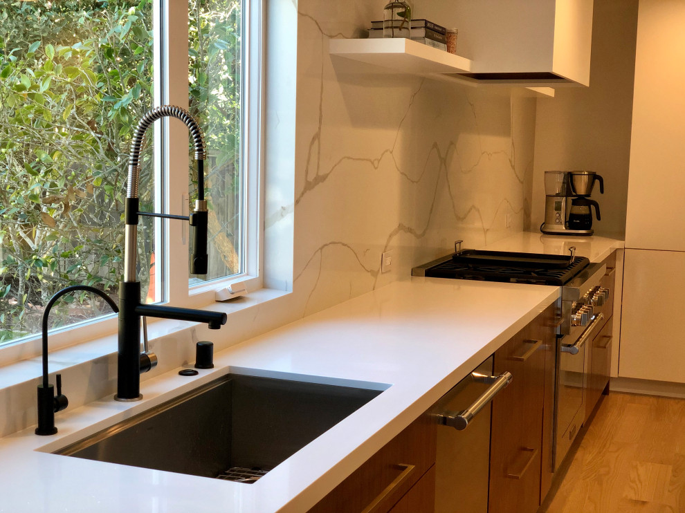 This is an example of a large modern l-shaped kitchen/diner in San Francisco with a submerged sink, flat-panel cabinets, medium wood cabinets, engineered stone countertops, white splashback, stone slab splashback, stainless steel appliances, light hardwood flooring, an island, grey floors and white worktops.