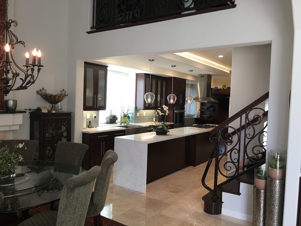 This is an example of a medium sized classic l-shaped kitchen/diner in Orange County with a belfast sink, glass-front cabinets, dark wood cabinets, marble worktops, grey splashback, glass tiled splashback, integrated appliances, travertine flooring and an island.