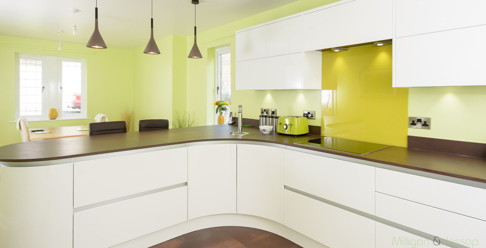 Bild på ett mellanstort funkis kök, med vita skåp, bänkskiva i koppar, grönt stänkskydd, glaspanel som stänkskydd och rostfria vitvaror