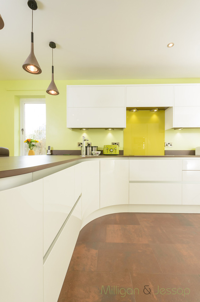 Foto på ett mellanstort funkis kök, med vita skåp, bänkskiva i koppar, grönt stänkskydd, glaspanel som stänkskydd och rostfria vitvaror