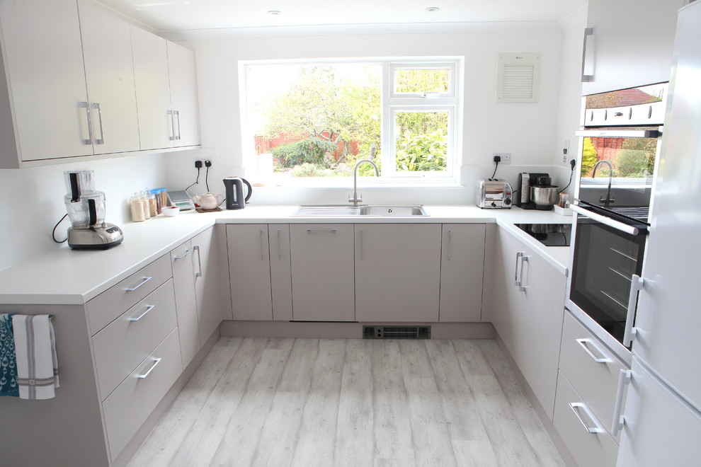 Inspiration for a medium sized modern u-shaped enclosed kitchen in Wiltshire with a built-in sink, flat-panel cabinets, beige cabinets, laminate countertops, multi-coloured splashback, black appliances, plywood flooring and no island.