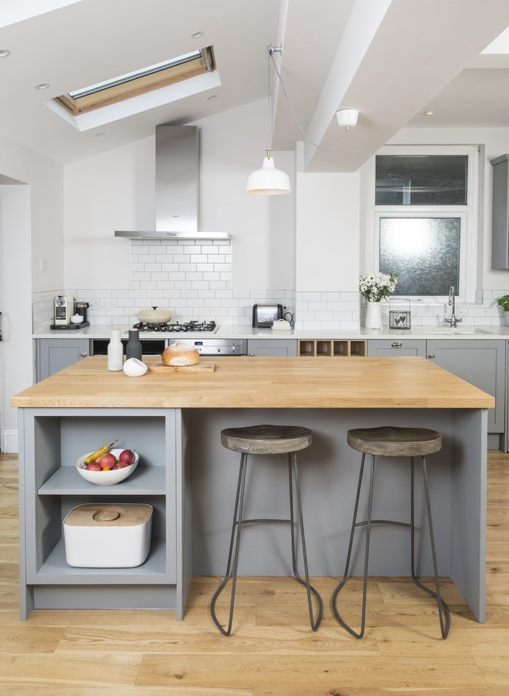 Farmhouse kitchen in Cardiff with grey cabinets, white splashback, metro tiled splashback, stainless steel appliances, light hardwood flooring and an island.