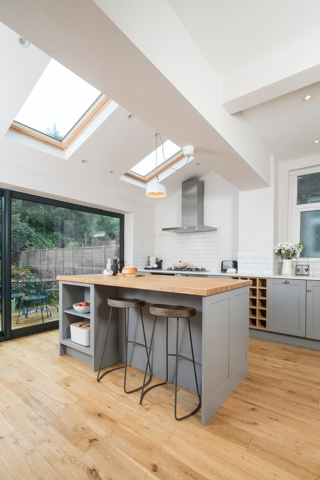 Small classic single-wall open plan kitchen in Cardiff with a submerged sink, shaker cabinets, grey cabinets, quartz worktops, white splashback, metro tiled splashback, stainless steel appliances, light hardwood flooring and an island.