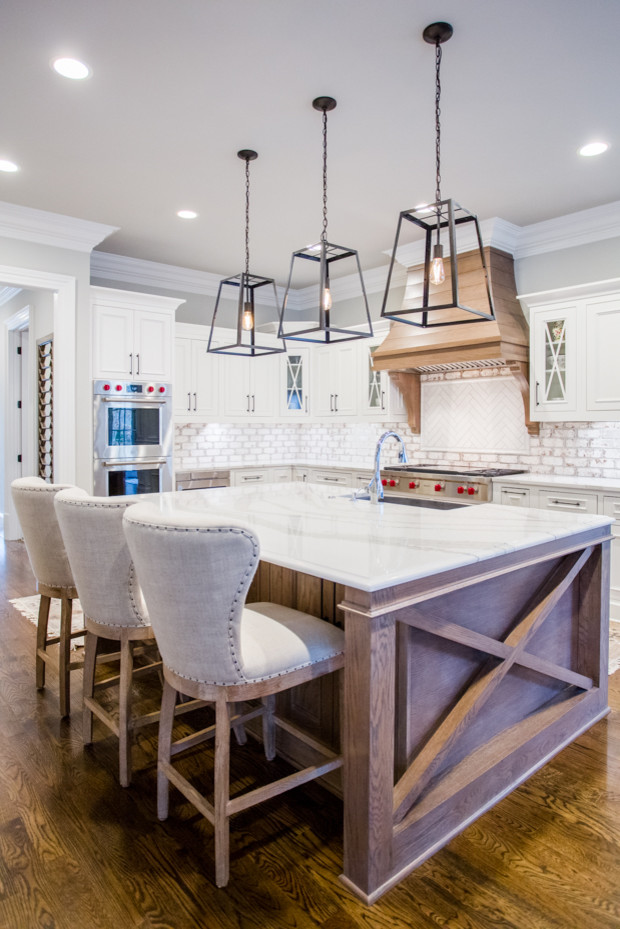 Eat-in kitchen - large transitional u-shaped medium tone wood floor and brown floor eat-in kitchen idea in Atlanta with a farmhouse sink, raised-panel cabinets, white cabinets, quartz countertops, white backsplash, brick backsplash, stainless steel appliances, an island and white countertops