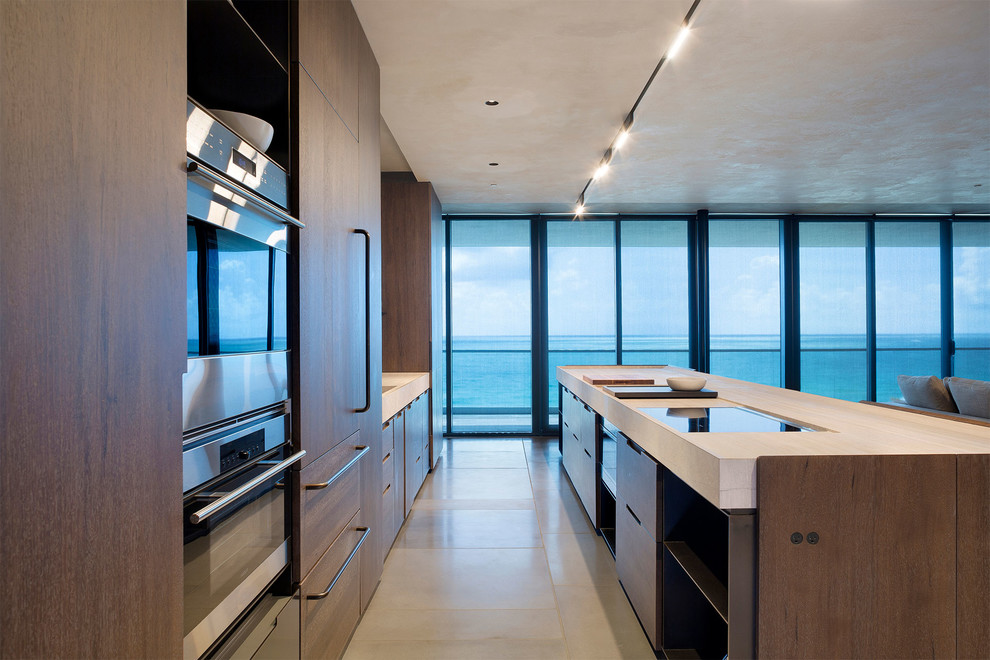 This is an example of a medium sized contemporary single-wall open plan kitchen in Miami with a submerged sink, flat-panel cabinets, medium wood cabinets, composite countertops, stainless steel appliances, porcelain flooring, an island, beige floors and beige worktops.