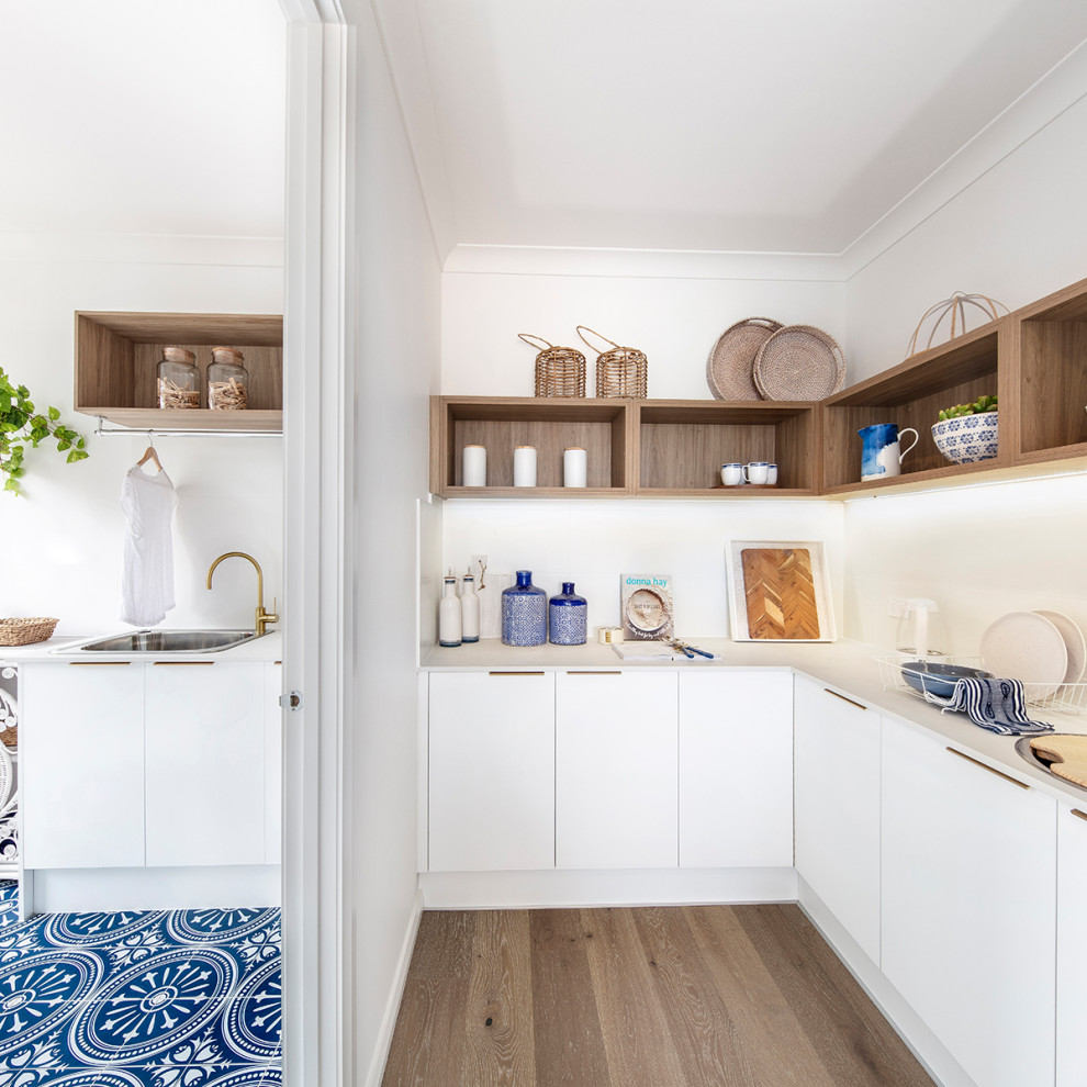 Photo of a medium sized nautical l-shaped kitchen pantry in Wollongong with shaker cabinets, white cabinets, engineered stone countertops, white splashback, ceramic splashback, light hardwood flooring, an island, brown floors and white worktops.