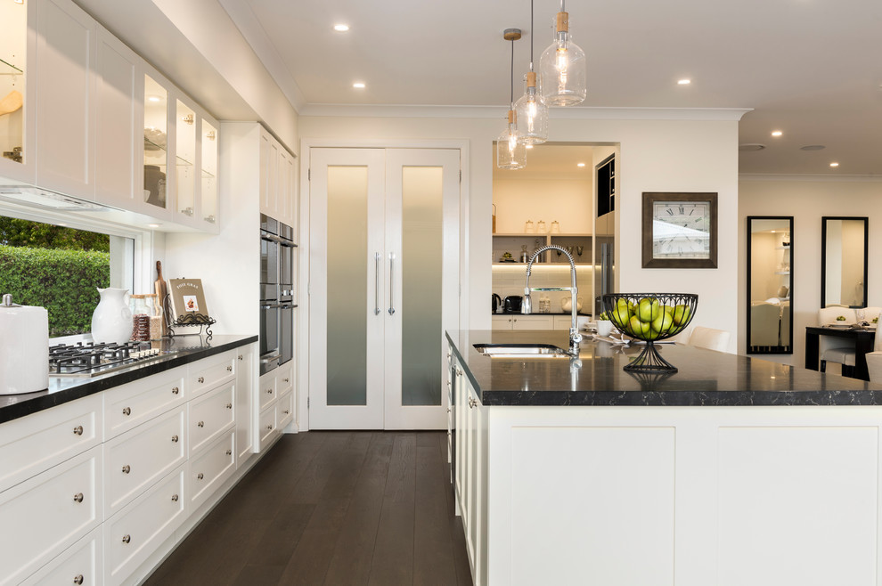 This is an example of a large contemporary galley open plan kitchen in Sydney with a submerged sink, white cabinets, window splashback, stainless steel appliances and an island.