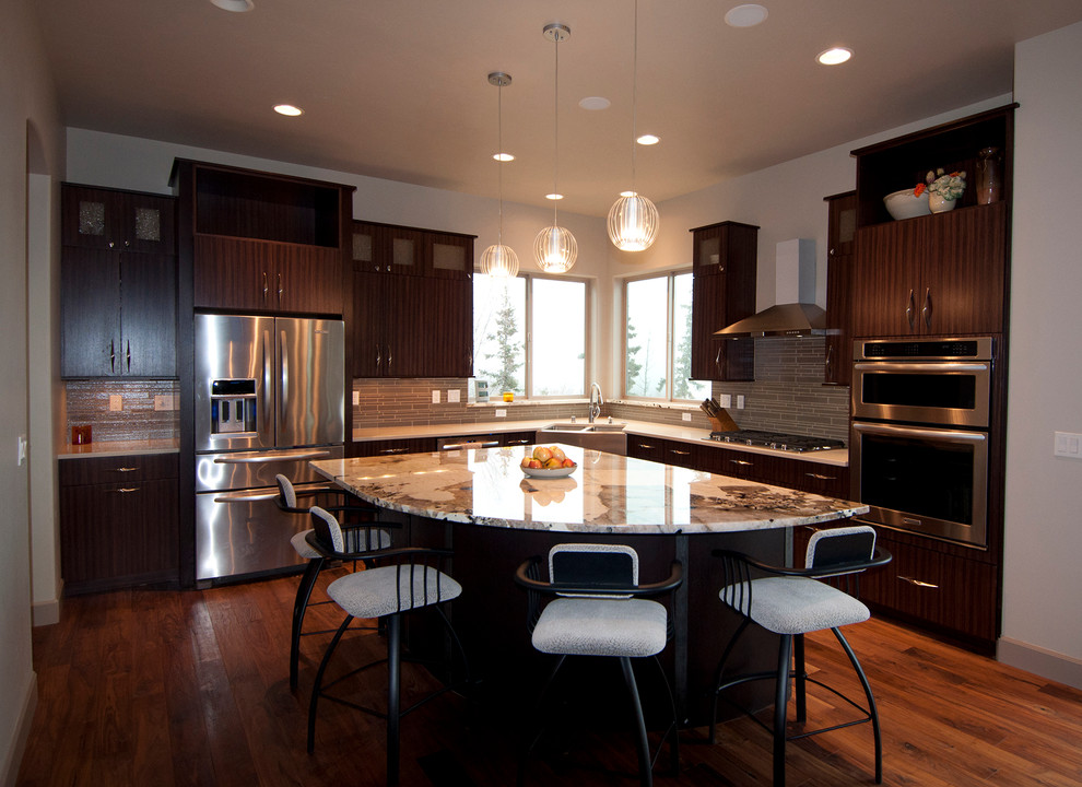 Example of a mid-sized trendy l-shaped medium tone wood floor eat-in kitchen design in Other with a farmhouse sink, flat-panel cabinets, dark wood cabinets, onyx countertops, gray backsplash, glass tile backsplash, stainless steel appliances and an island