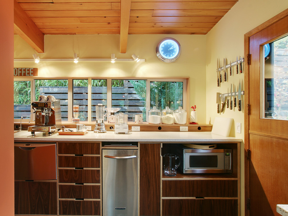 Foto på ett stort kök och matrum, med släta luckor, skåp i mörkt trä, bänkskiva i återvunnet glas och rostfria vitvaror