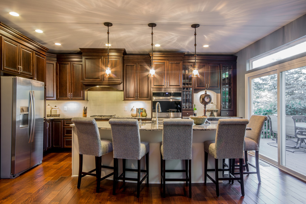 Inspiration for a large timeless l-shaped medium tone wood floor eat-in kitchen remodel in Detroit with an undermount sink, raised-panel cabinets, dark wood cabinets, quartz countertops, beige backsplash, ceramic backsplash, stainless steel appliances and an island