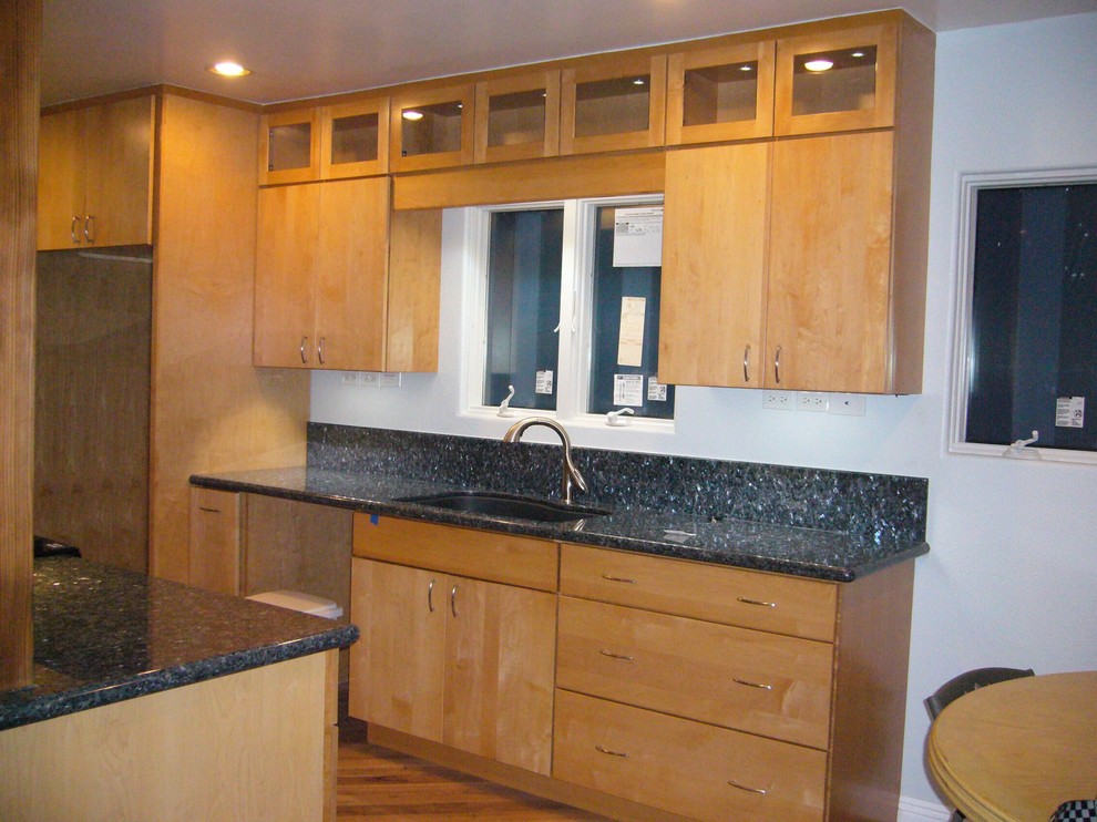 Ejemplo de cocina comedor moderna con fregadero bajoencimera, armarios con paneles lisos, puertas de armario de madera clara, encimera de granito y electrodomésticos negros