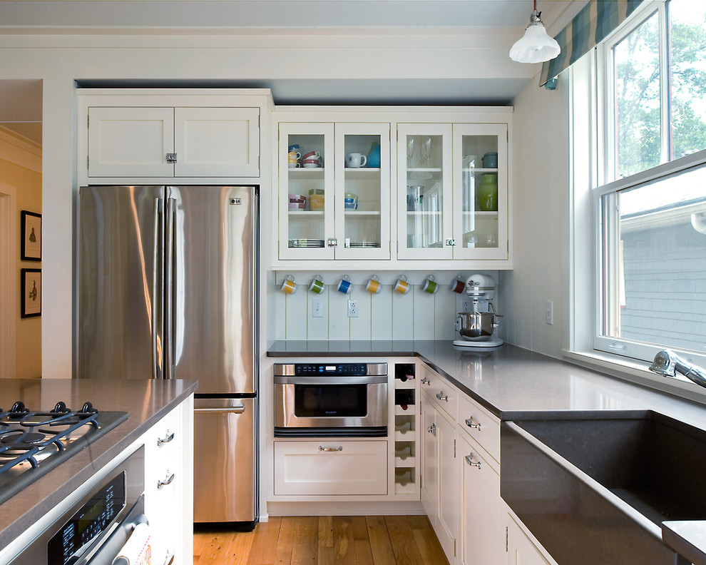 Inspiration for a mid-sized timeless u-shaped light wood floor eat-in kitchen remodel in Detroit with a farmhouse sink, stainless steel appliances, quartz countertops, white cabinets, white backsplash, an island and shaker cabinets