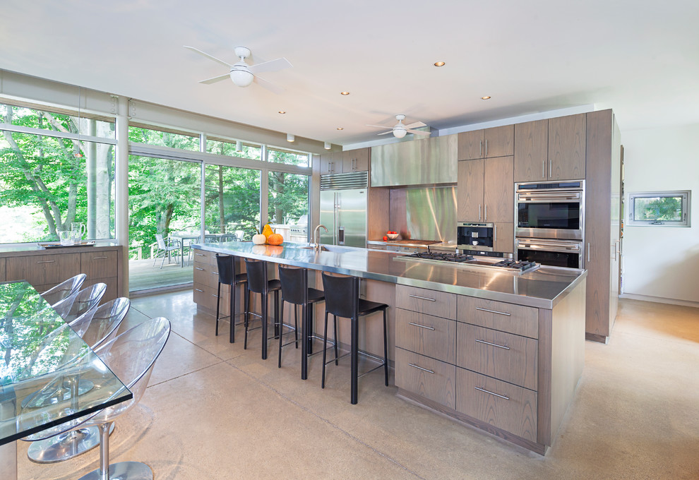 Example of a large trendy galley concrete floor eat-in kitchen design in Grand Rapids with flat-panel cabinets, stainless steel countertops, metallic backsplash, stainless steel appliances, an island and medium tone wood cabinets