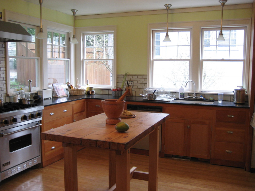 This is an example of a small traditional l-shaped enclosed kitchen in Seattle with a submerged sink, flat-panel cabinets, light wood cabinets, granite worktops, white splashback, ceramic splashback, stainless steel appliances and light hardwood flooring.