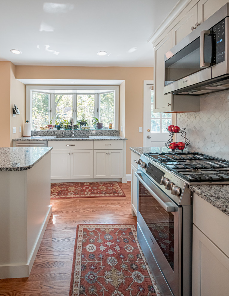 Foto på ett mellanstort vintage kök, med en undermonterad diskho, skåp i shakerstil, granitbänkskiva, vitt stänkskydd, stänkskydd i marmor, rostfria vitvaror, mellanmörkt trägolv och en köksö