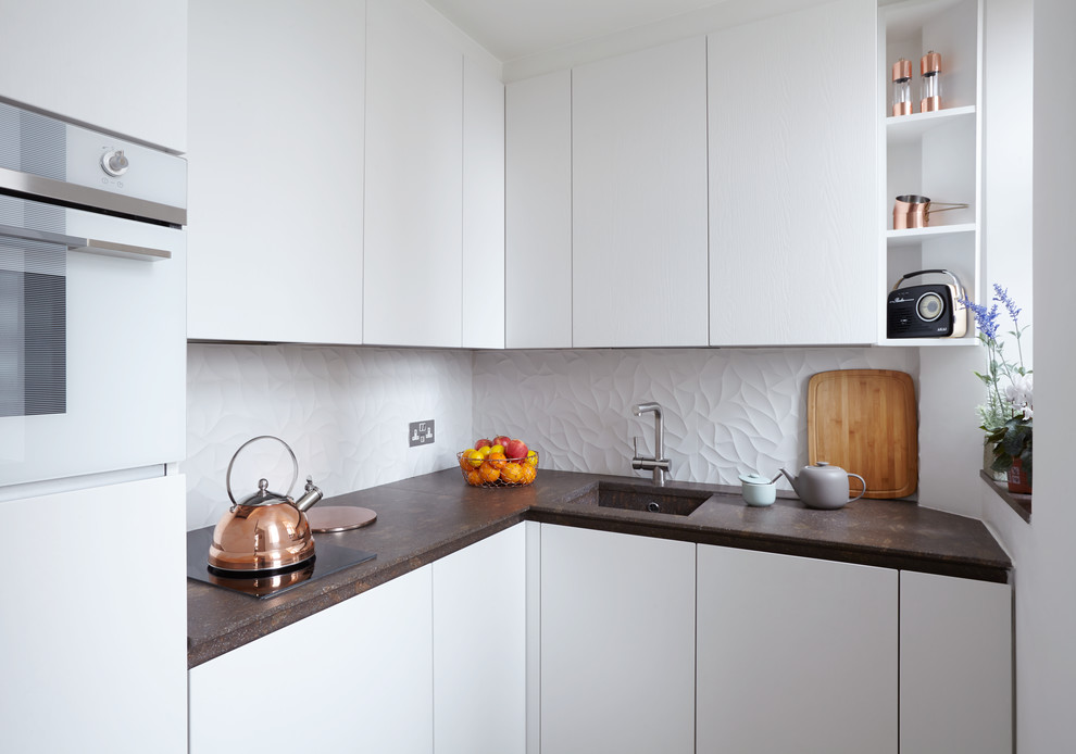 This is an example of a small retro l-shaped enclosed kitchen in London with a built-in sink, flat-panel cabinets, white cabinets, granite worktops, white splashback, ceramic splashback, integrated appliances and no island.