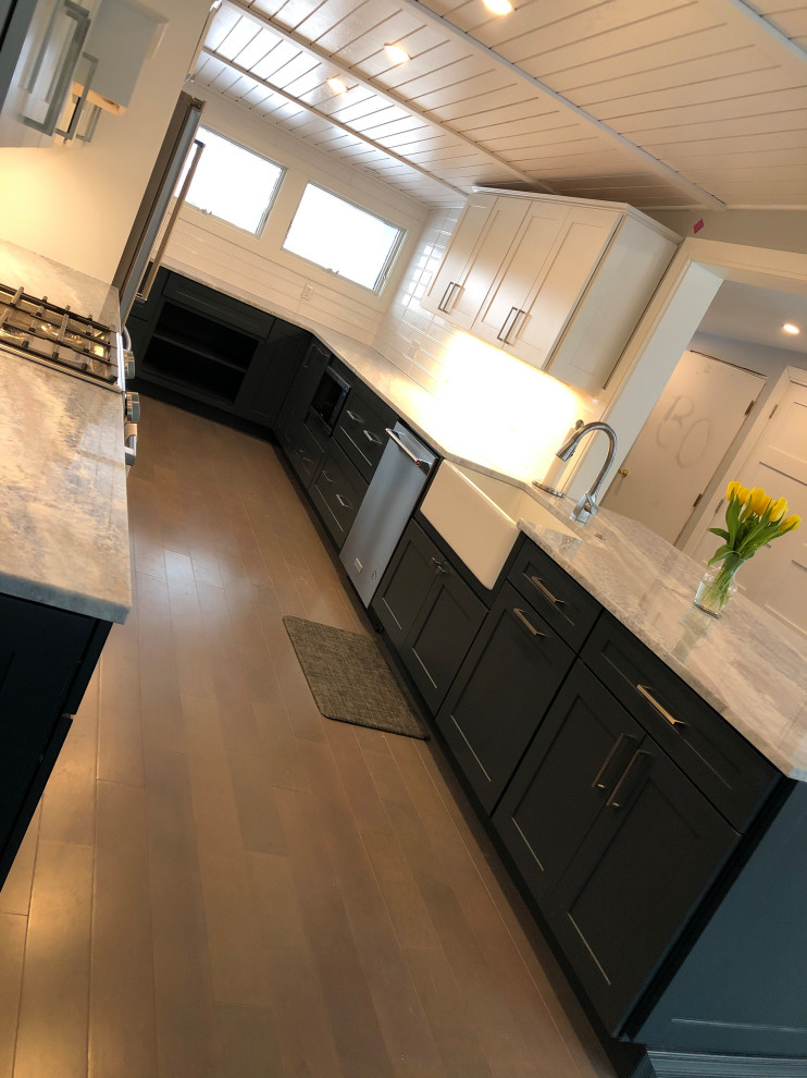 This is an example of a large retro l-shaped kitchen/diner in New York with a belfast sink, shaker cabinets, blue cabinets, granite worktops, white splashback, metro tiled splashback, stainless steel appliances, light hardwood flooring, no island, grey floors, grey worktops and a wood ceiling.