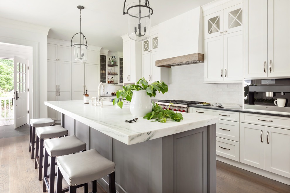 Exempel på ett klassiskt vit vitt kök, med marmorbänkskiva, vitt stänkskydd, en köksö, en undermonterad diskho, skåp i shakerstil, vita skåp, stänkskydd i tunnelbanekakel, rostfria vitvaror och mellanmörkt trägolv