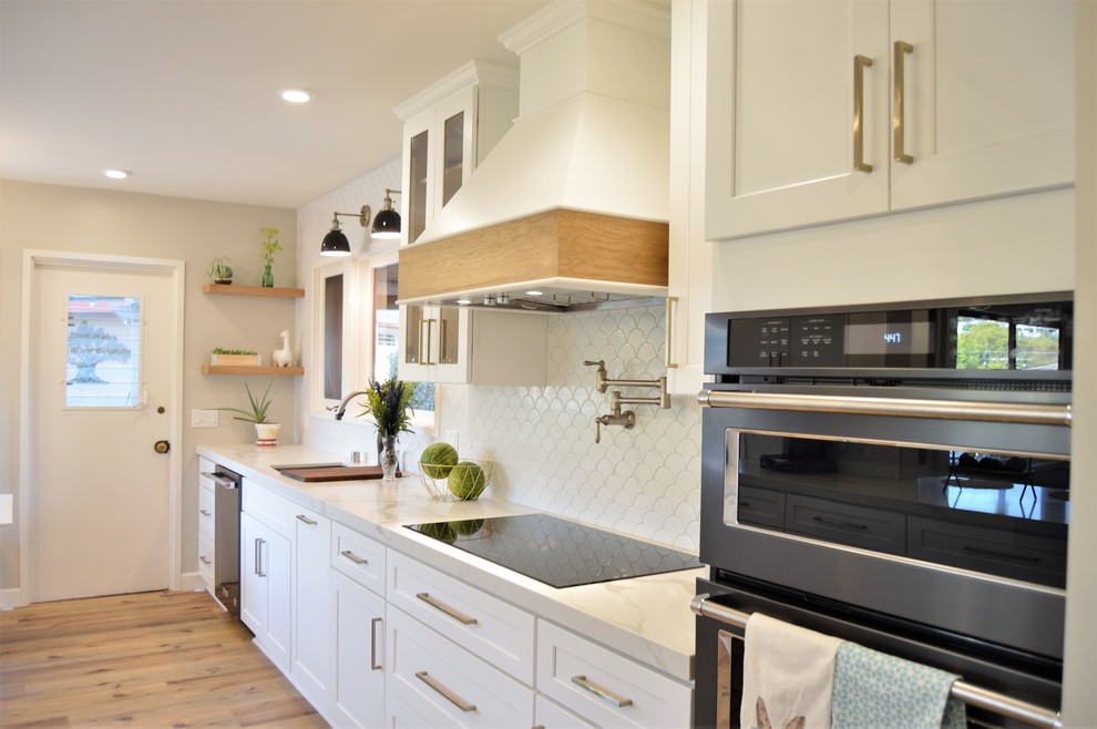 Exempel på ett stort retro vit vitt kök, med en undermonterad diskho, skåp i shakerstil, vita skåp, bänkskiva i kvarts, vitt stänkskydd, stänkskydd i porslinskakel, svarta vitvaror, laminatgolv, en halv köksö och brunt golv