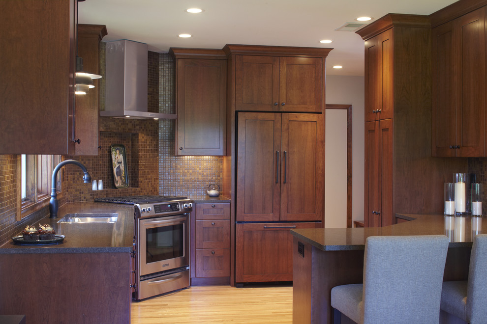 Bild på ett 50 tals kök, med en undermonterad diskho, skåp i mörkt trä, bänkskiva i kvarts, brunt stänkskydd, stänkskydd i mosaik och integrerade vitvaror