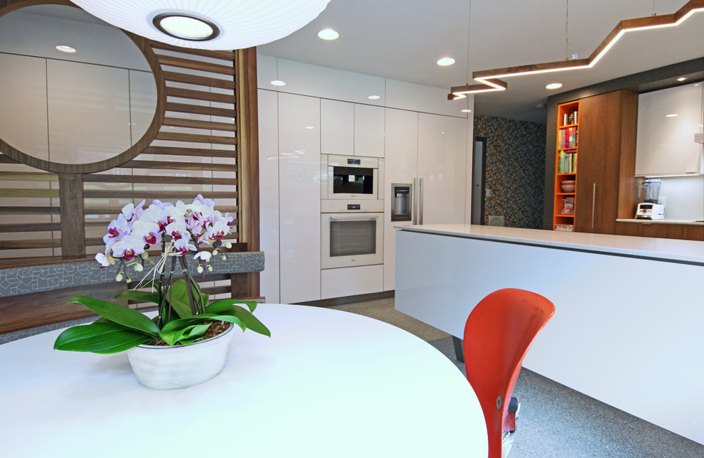 Photo of a medium sized retro l-shaped kitchen/diner in Charlotte with a submerged sink, flat-panel cabinets, white cabinets, quartz worktops, white splashback, white appliances, terrazzo flooring, an island, grey floors and white worktops.