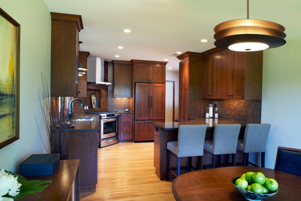 Bild på ett 60 tals kök, med en undermonterad diskho, skåp i mörkt trä, bänkskiva i kvarts, brunt stänkskydd, stänkskydd i mosaik, integrerade vitvaror, mellanmörkt trägolv och en halv köksö