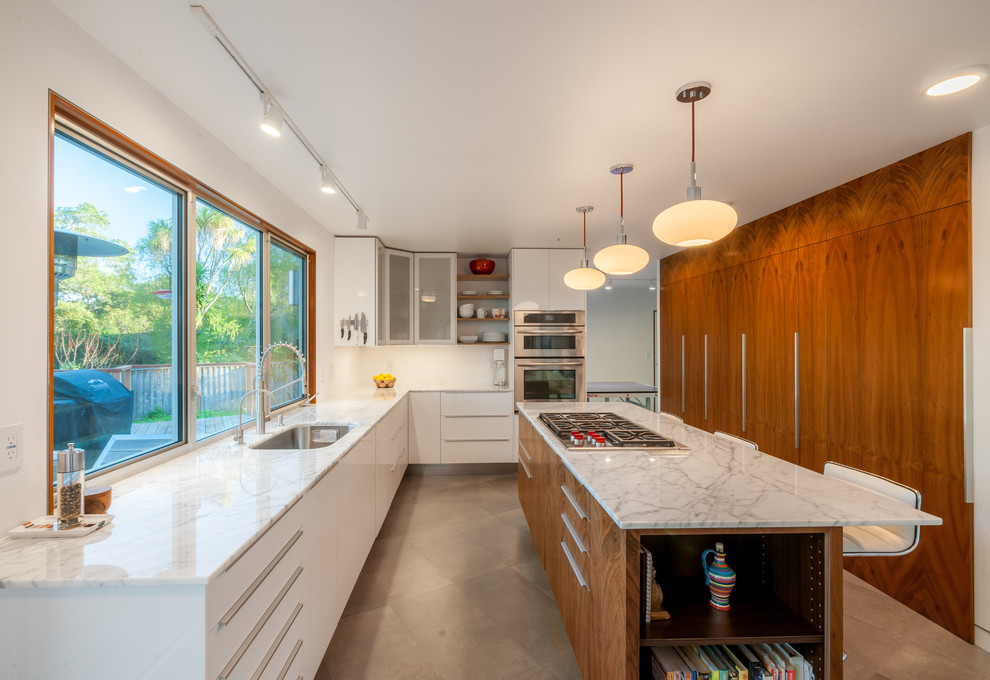 Bild på ett mellanstort 50 tals kök, med en undermonterad diskho, släta luckor, vita skåp, marmorbänkskiva, rostfria vitvaror, cementgolv och en köksö