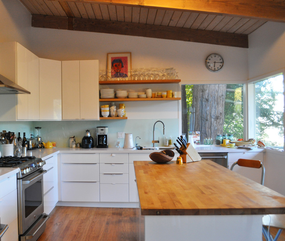 Diseño de cocinas en L moderna de tamaño medio abierta con electrodomésticos de acero inoxidable, salpicadero de vidrio templado, fregadero bajoencimera, armarios con paneles lisos, puertas de armario de madera oscura, encimera de cuarzo compacto, salpicadero blanco, suelo de madera oscura y una isla