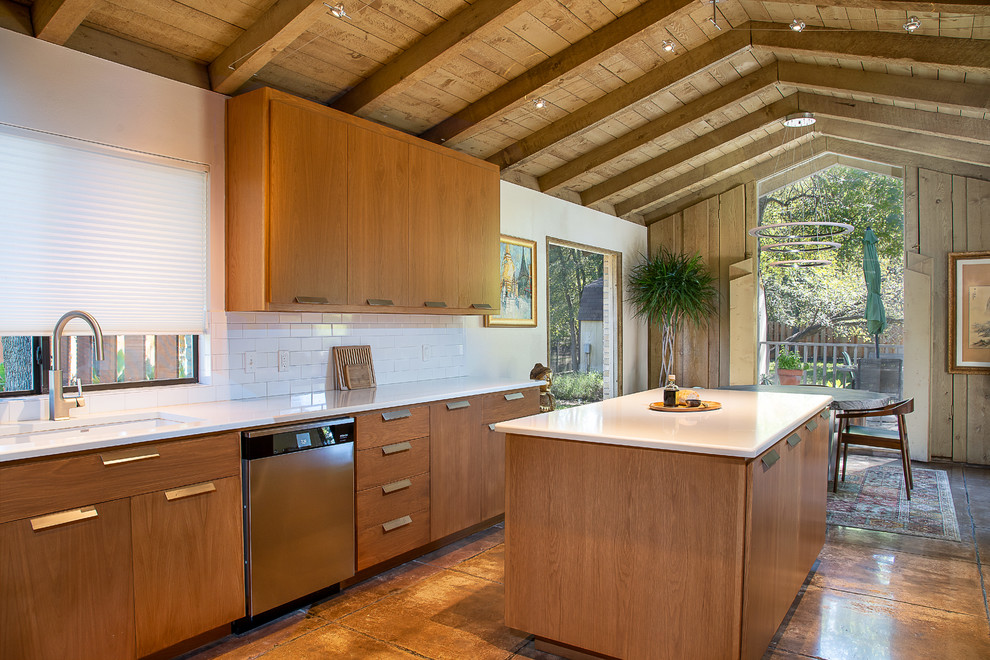 Foto på ett 60 tals vit kök och matrum, med en undermonterad diskho, släta luckor, skåp i mellenmörkt trä, vitt stänkskydd, stänkskydd i tunnelbanekakel, rostfria vitvaror, en köksö och brunt golv