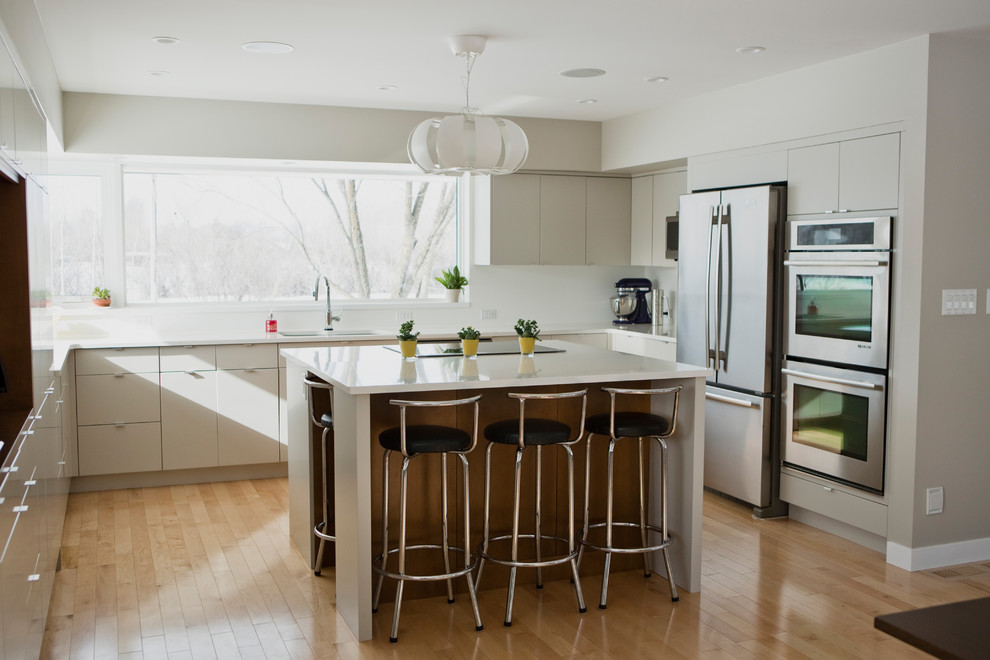 Immagine di una cucina design con lavello sottopiano, ante lisce, ante bianche, elettrodomestici in acciaio inossidabile, parquet chiaro, pavimento beige e top bianco