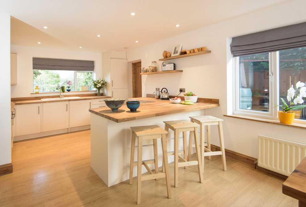 Einzeilige, Mittelgroße Moderne Wohnküche mit weißen Schränken, Arbeitsplatte aus Holz, braunem Holzboden, Halbinsel, Einbauwaschbecken, Lamellenschränken und Küchenrückwand in Weiß in Cambridgeshire