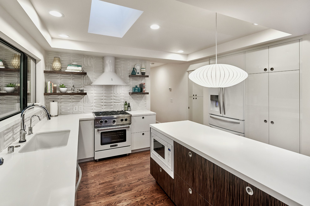 Bild på ett mellanstort 60 tals kök, med en undermonterad diskho, släta luckor, vita skåp, vitt stänkskydd, vita vitvaror, mörkt trägolv, en köksö, brunt golv och bänkskiva i kvartsit