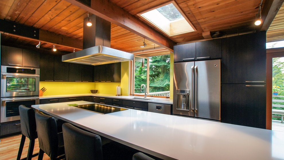 Photo of a medium sized midcentury l-shaped kitchen/diner in Seattle with a submerged sink, yellow splashback, stainless steel appliances, an island, flat-panel cabinets, brown cabinets, engineered stone countertops, stone slab splashback and light hardwood flooring.