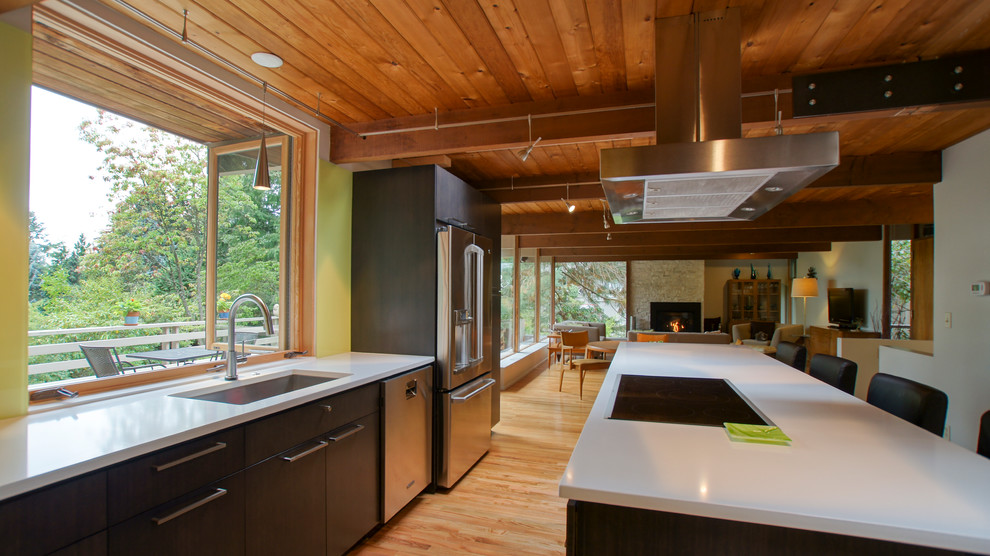 Foto på ett mellanstort retro kök, med en undermonterad diskho, gult stänkskydd, ljust trägolv, en köksö, rostfria vitvaror, släta luckor, bruna skåp, bänkskiva i kvarts och stänkskydd i sten