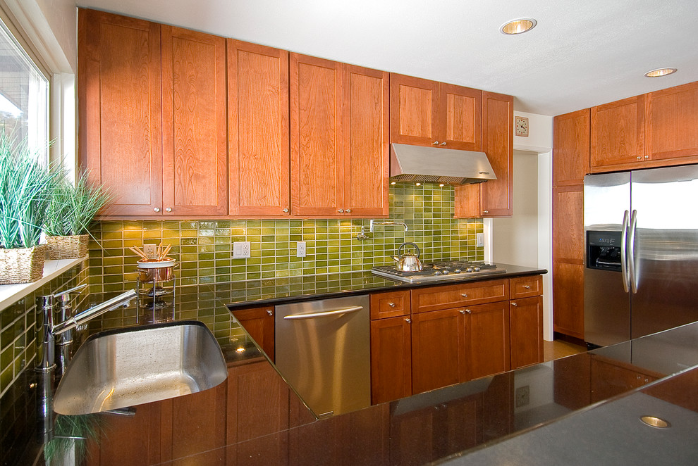 Exempel på ett 50 tals u-kök, med en nedsänkt diskho, skåp i shakerstil, skåp i mellenmörkt trä, granitbänkskiva, grönt stänkskydd, stänkskydd i keramik, rostfria vitvaror och korkgolv