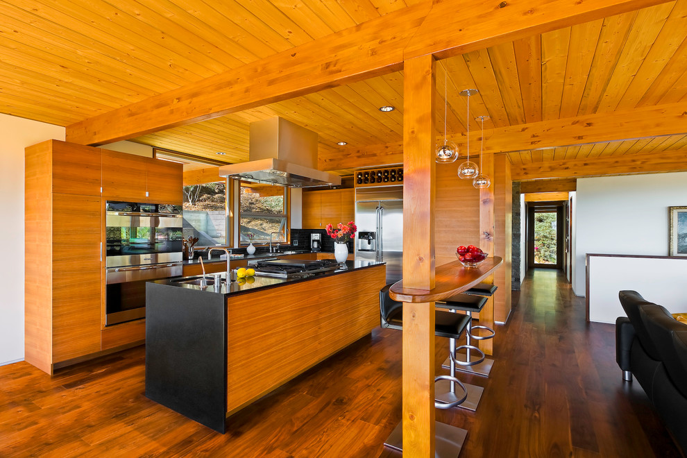 Foto på ett stort 60 tals svart linjärt kök med öppen planlösning, med brunt golv, en undermonterad diskho, släta luckor, skåp i mellenmörkt trä, rostfria vitvaror, mellanmörkt trägolv och en köksö