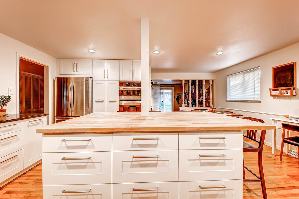 Inredning av ett retro mellanstort kök, med grönt stänkskydd, rostfria vitvaror, en enkel diskho, luckor med infälld panel, vita skåp, träbänkskiva, glaspanel som stänkskydd, mellanmörkt trägolv och en köksö
