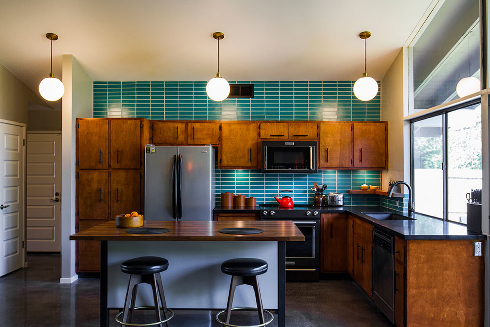 Exempel på ett klassiskt l-kök, med skåp i mörkt trä, grönt stänkskydd, stänkskydd i keramik, en köksö, en undermonterad diskho, släta luckor, svarta vitvaror och brunt golv