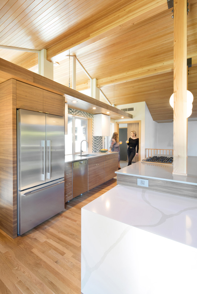Immagine di una cucina moderna con lavello sottopiano, ante lisce, top in quarzo composito, paraspruzzi verde, paraspruzzi con piastrelle di vetro, elettrodomestici in acciaio inossidabile e pavimento in legno massello medio