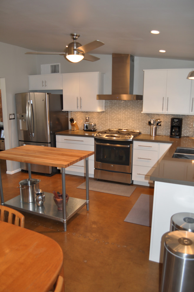 Bild på ett mellanstort retro kök, med en undermonterad diskho, släta luckor, vita skåp, bänkskiva i kvarts, grått stänkskydd, stänkskydd i glaskakel, rostfria vitvaror, betonggolv och en köksö