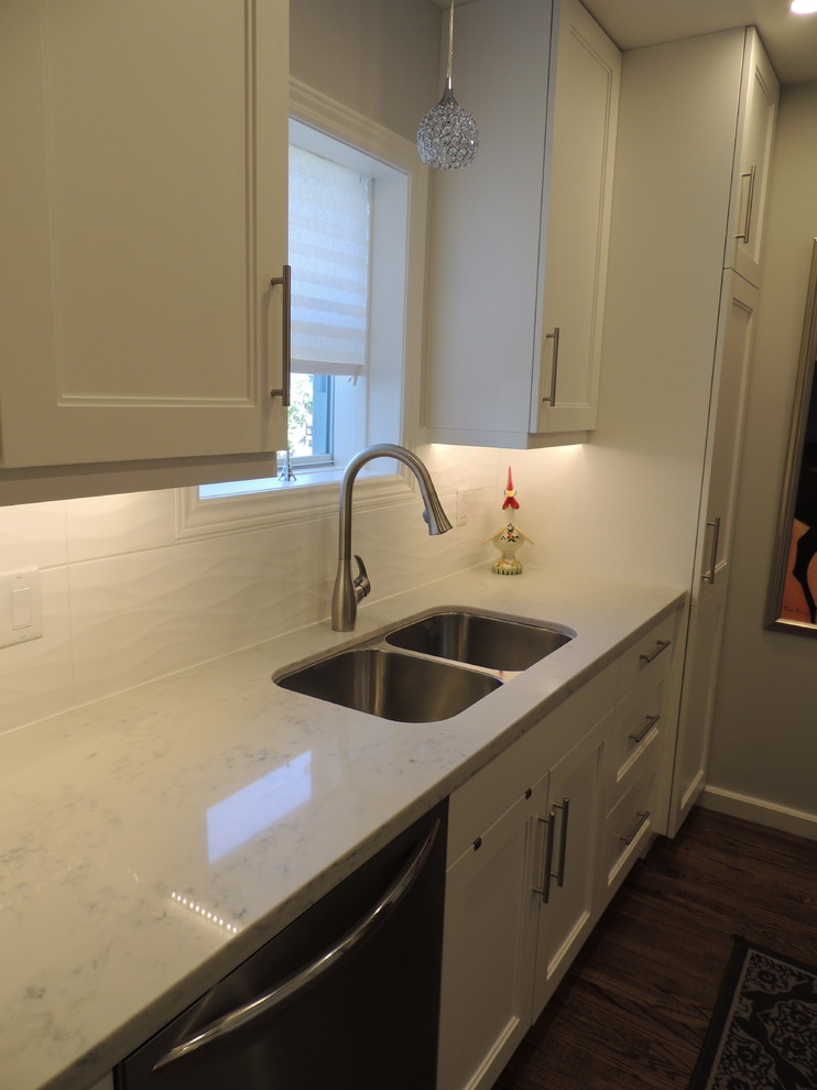 Photo of a small traditional galley enclosed kitchen in Toronto with a submerged sink, shaker cabinets, white cabinets, engineered stone countertops, white splashback, porcelain splashback, stainless steel appliances, medium hardwood flooring and no island.