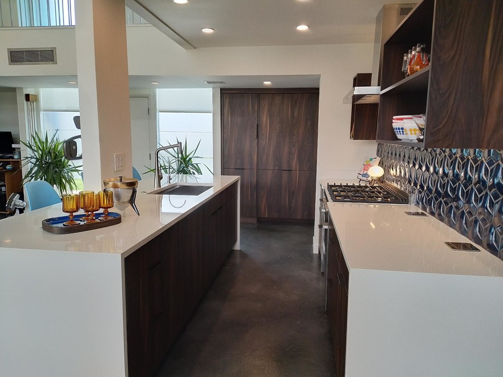 Example of a small mid-century modern single-wall concrete floor and gray floor open concept kitchen design in Other with an undermount sink, flat-panel cabinets, dark wood cabinets, quartz countertops, metallic backsplash, porcelain backsplash, paneled appliances, an island and white countertops