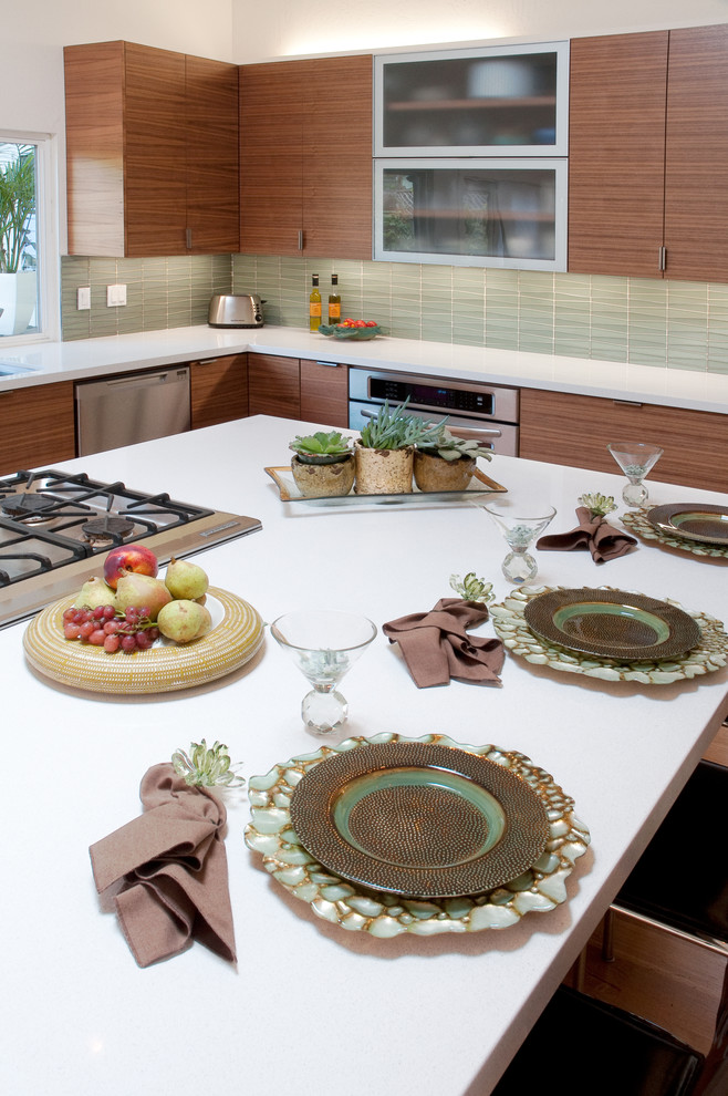 Eat-in kitchen - 1950s l-shaped light wood floor eat-in kitchen idea in San Francisco with an undermount sink, flat-panel cabinets, medium tone wood cabinets, solid surface countertops, green backsplash, stainless steel appliances, an island and glass tile backsplash