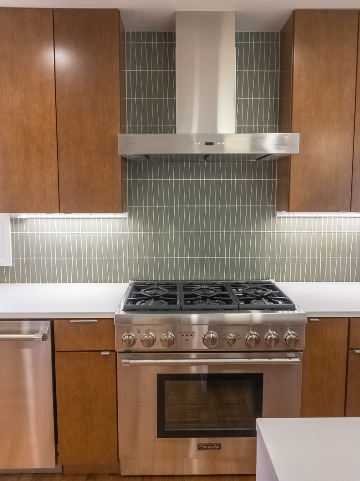 Foto på ett stort 50 tals kök, med en undermonterad diskho, släta luckor, skåp i mellenmörkt trä, bänkskiva i kvarts, grönt stänkskydd, stänkskydd i glaskakel, rostfria vitvaror, mellanmörkt trägolv och en köksö