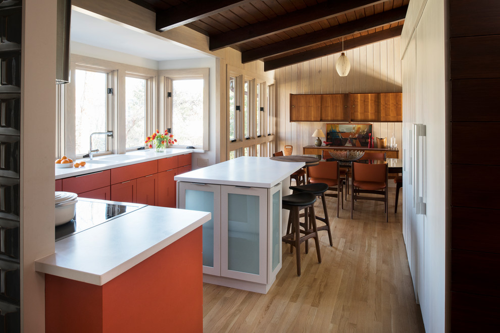 Mittelgroße Mid-Century Wohnküche in L-Form mit Schrankfronten im Shaker-Stil, orangefarbenen Schränken, Mineralwerkstoff-Arbeitsplatte, Kücheninsel, Doppelwaschbecken, Küchengeräten aus Edelstahl und hellem Holzboden in Atlanta