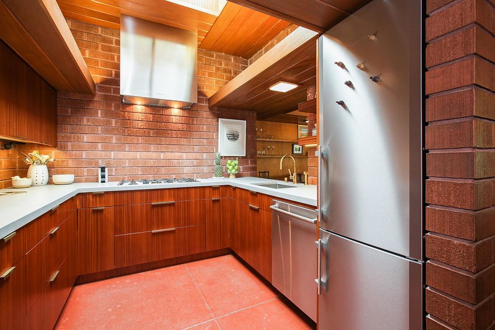 Bild på ett avskilt, litet funkis vit vitt u-kök, med en undermonterad diskho, släta luckor, skåp i mellenmörkt trä, bänkskiva i kvarts, brunt stänkskydd, stänkskydd i tegel, rostfria vitvaror, klinkergolv i keramik och brunt golv