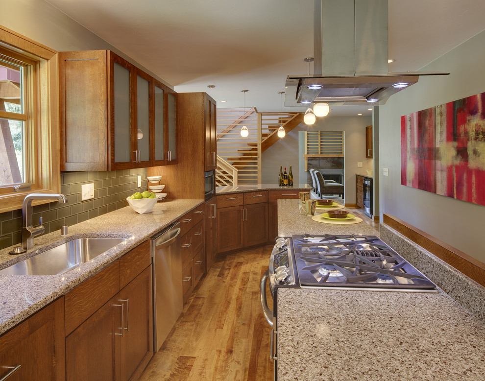 Photo of a retro galley kitchen/diner in Milwaukee with a submerged sink, glass-front cabinets, medium wood cabinets, engineered stone countertops, grey splashback, glass tiled splashback, stainless steel appliances, medium hardwood flooring and an island.