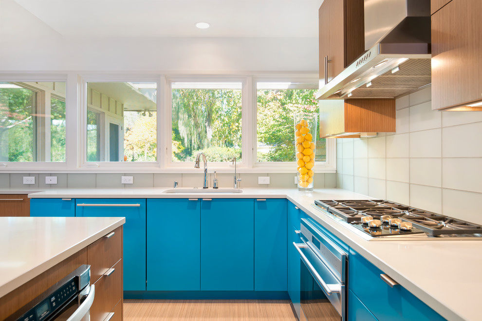 Modern inredning av ett avskilt u-kök, med en undermonterad diskho, släta luckor, blå skåp, bänkskiva i kvartsit, stänkskydd i glaskakel och rostfria vitvaror